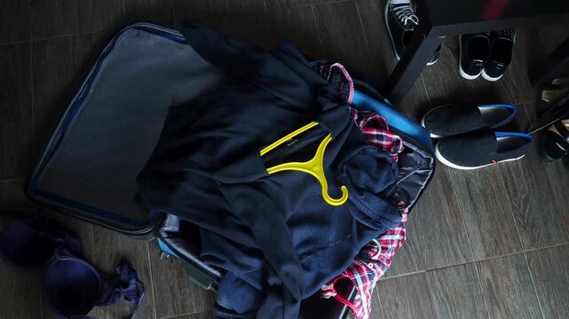 A woman packs suitcase and zips up suitcase zipper, takes the travel bag away. Tracking with high angle of unrecognizable person putting clothes