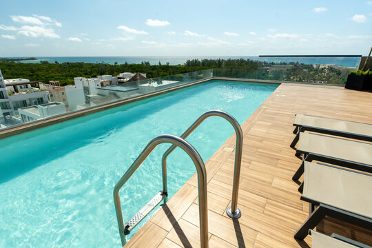 Terraza con alberca y camastros en rooftop de lujo con vista panor&aacute;mica al mar en d&iacute;a soleado. Arquitectura moderna de resort tropical.