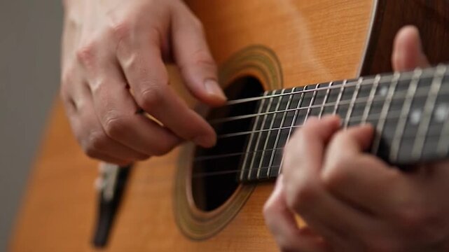 A person hands are shown playing a wooden acoustic guitar, close-up view of the instrument and fingers plucking the strings