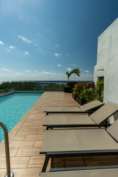 Terraza con alberca y camastros en rooftop de lujo con vista panor&aacute;mica al mar en d&iacute;a soleado. Arquitectura moderna de resort tropical.
