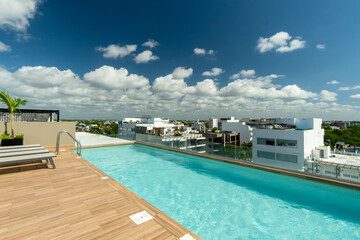 Fototapeta premium Terraza con alberca y camastros en rooftop de lujo con vista panorámica al mar en día soleado. Arquitectura moderna de resort tropical.