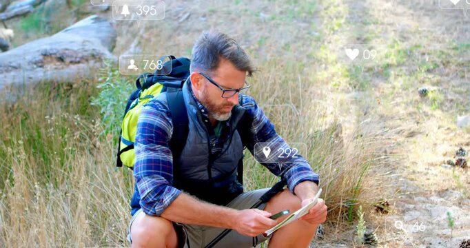 Hiker crouching on trail, tapping tablet with stylus checking route and causing social media alerts