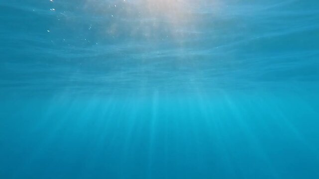 A captivating close-up showing radiant sun rays piercing through the ripples of clear blue sea water, creating a stunning and serene underwater scene.