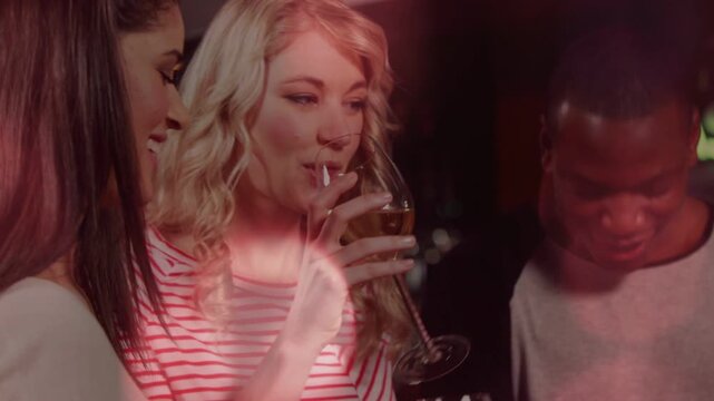 Blonde woman leading toast, friends raising glasses and cheering at bar, bokeh drifting over faces