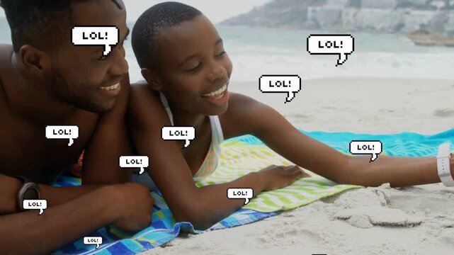 Couple on towel by sea holding phone, laughing for social, causing LOL bubbles overlaying subjects