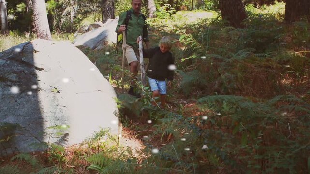 Child starting descent off boulder, parent following and guiding with staff, ensuring safe hike