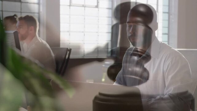 Man using laptop in office, gavel graphic drifting over face and torso, signaling legal decision