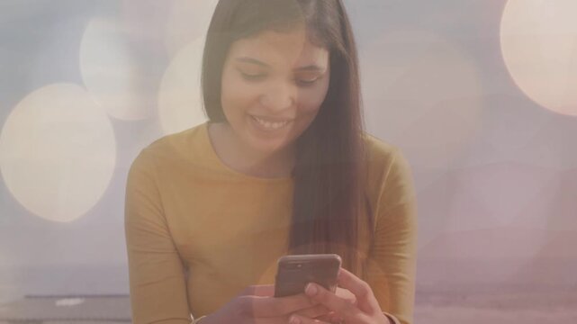 Woman sitting tapping phone reading and typing, tech bokeh overlays floating around her on roof