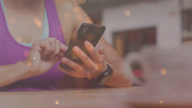 Woman tapping phone at table and checking messages in tech, warm bokeh growing and obscuring frame