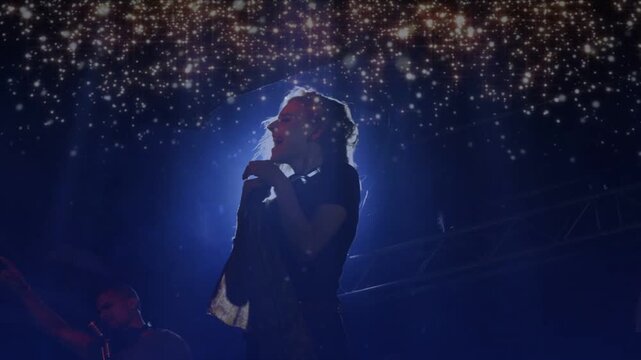 Lead singer hair flipping, leaning into mic, holding note while gold sparks framing music stage