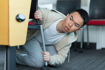 An Asian young man hides under a desk active shooter drill in a classroom, perfect for school safety, emergency preparedness, or campus security concepts. © fotolite