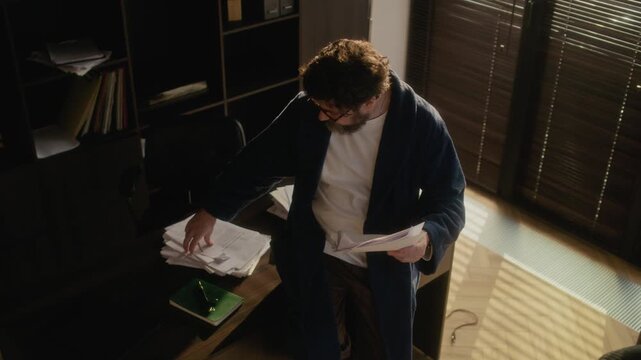 High angle view of middle aged male writer sitting on table in home office reading novel typescript, copy space