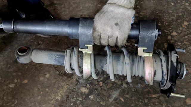 Gloved hand holding a car shock absorber with compressed spring