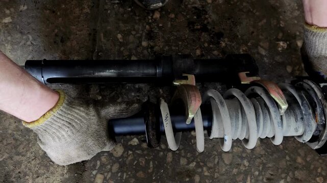 Gloved hand holding a car shock absorber with compressed spring
