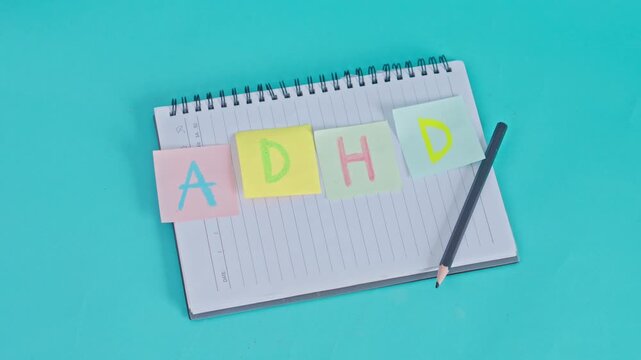 Mental health flat lay featuring ADHD lettering on notes with pencil and notepad on turquoise surface