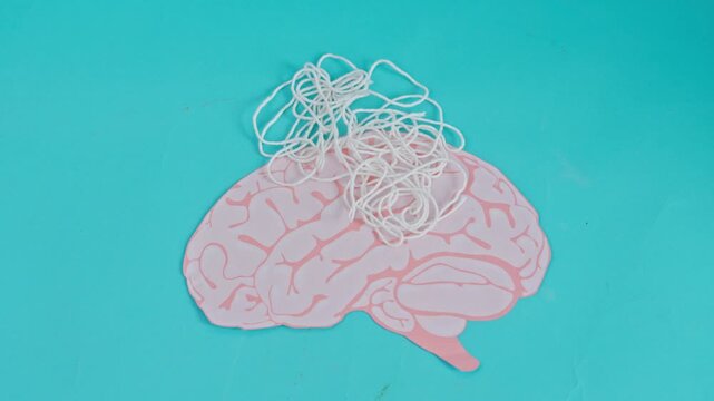 Pink paper brain with tangled white string on turquoise background for mental confusion or ADHD