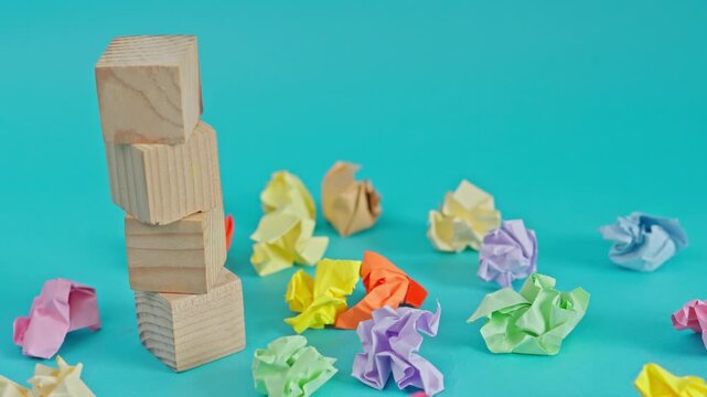 Stop motion of wooden blocks stacking and gone amidst colorful crumpled papers on turquoise background