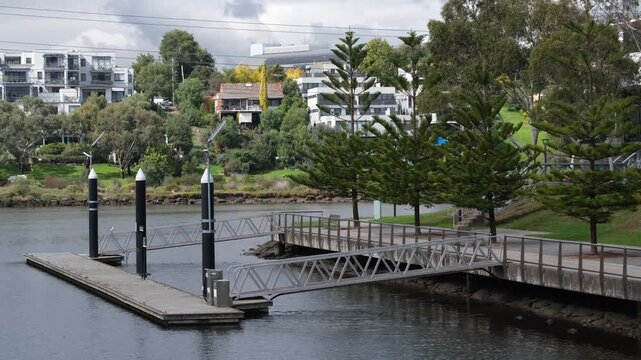 A public boat pontoon and aluminium gangway access ramp on the Maribyrnong River in Melbourne Australia. Riverside recreational amenity, walking path and waterfront houses.