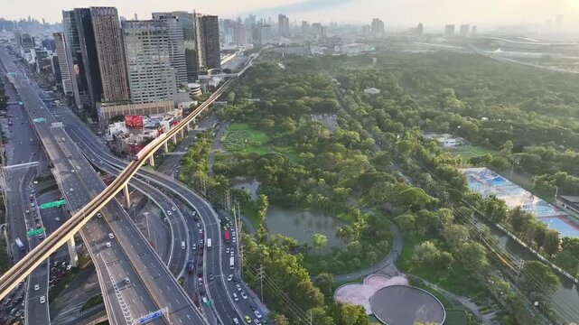 Chatuchak Park with dense trees ponds and walking paths beside city buildings. Green space contrasts with surrounding urban environment.