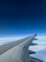 Obraz premium View from Airplane Window Showing Wing and Clouds During Flight.Airplane Wing View Above Clouds with Blue Sky from Window Seat. 