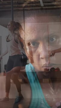 Vertical video: Woman in teal tank punching at lens while rope jumper causing closeup blend for gym