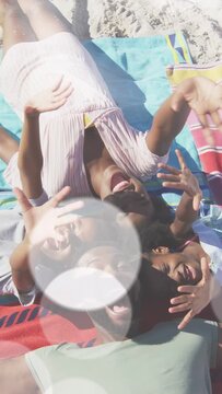Vertical video: Family turning to drone, reaching and laughing on towels, lensflare for travel