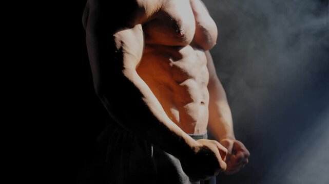 A male bodybuilder poses in shorts, showing off his muscles. Close-up of his chest and abs.
