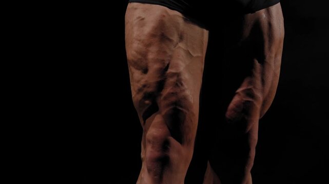 A male bodybuilder poses in shorts, showing off his leg muscles.