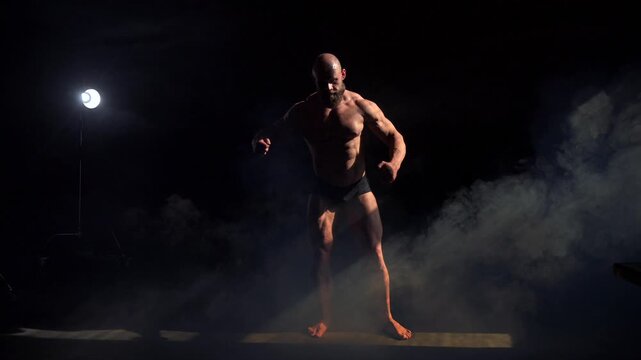 A male bodybuilder poses in shorts, showing off his muscles. 