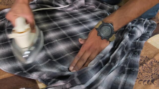 Close up of hands using an electric steam iron to remove wrinkles from clothing