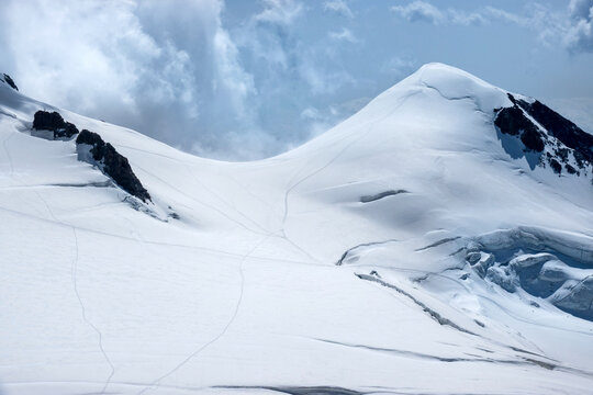 Snow Covered Alpine Peak with Glacier Crevasses and Dramatic Cloudy Sky Spaghetti Tour Route Rifugio Gnifetti Alagna Valsesia, Piedmont / Italy - July 19 2023: 