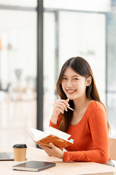 Happy Asian Female Freelancer Holding Notebook and Working in Cafe