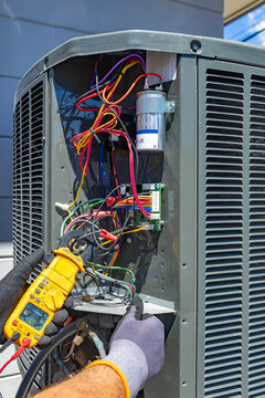 HVAC technician using a clamp meter to measure load current on an outdoor AC unit, USA