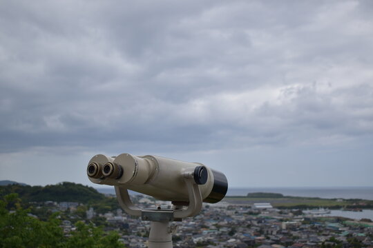 Tourist binoculars overlooking a coastal town and sea under overcast sky.