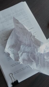 Vertical from above view of crumpled paper with novel draft on wooden table surface in writers office