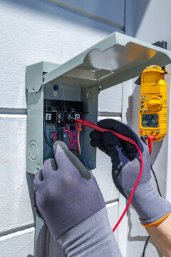 Electrician testing voltage in an outdoor 60 amp A/C electrical disconnect box with a multimeter, USA