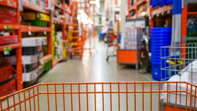 Shopping cart in foreground with blurred shelves of home improvement supplies in a large retail store interior