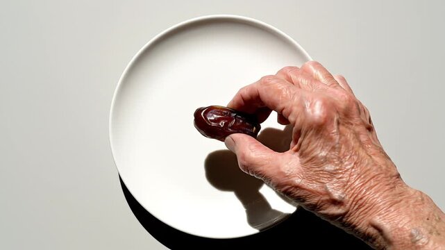 Senior hand picks up a single dried date from a white plate on table