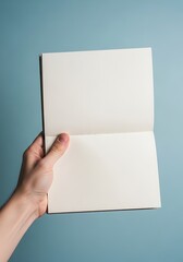Fototapeta premium Hand Holding an Open Blank Notebook with Empty Pages on Blue Background