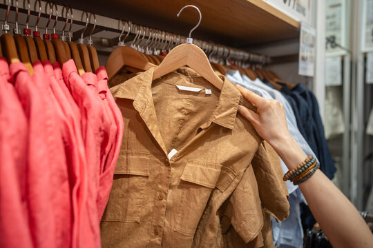 Woman shopper picking shirt on hanger from display at fashion clothing store, female client choosing clothing, checking color appearance and size of item, fashionable showroom offers trendy apparel.