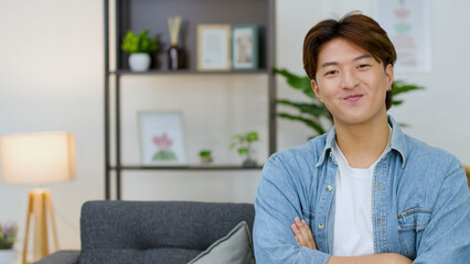 Fototapeta premium Smiling Young Asian Man with Arms Crossed in Modern Living Room