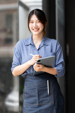 Smiling Asian cafe owner holding tablet and stylus