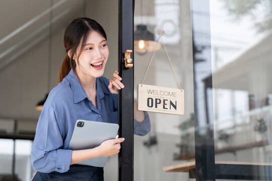 Young Asian cafe owner opening shop with welcome sign
