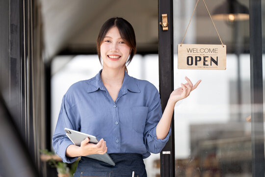 Cheerful Asian cafe owner presenting open sign