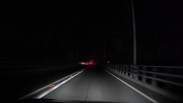 Dashcam point of view driving at night on a highway. Visible road markings, traffic signs and car lights ahead. Concept of transportation, road safety and night driving conditions.