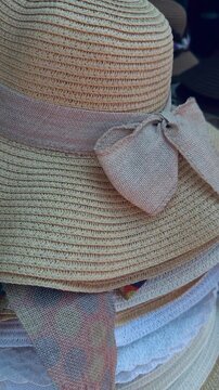 Close-up of stylish straw sun hats with ribbons and bows stacked for sale at a tropical market. Concept of summer fashion, beach accessories, and vacation shopping.