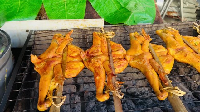 Traditional Thai street food Gai Yang: whole grilled chickens on bamboo skewers roasting over hot charcoal. Authentic Asian barbecue concept for travel, food, and culinary projects.