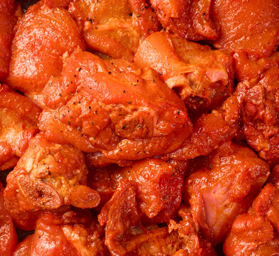 raw meat pieces coated in red spice marinade, textured moist meat surface, top view in full frame culinary background