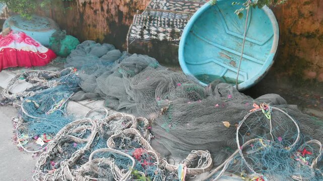 Fishing nets and ropes are piled up next to a blue boat in a harbor in Nha Trang, Vietnam. The equipment is ready for the next fishing trip.
