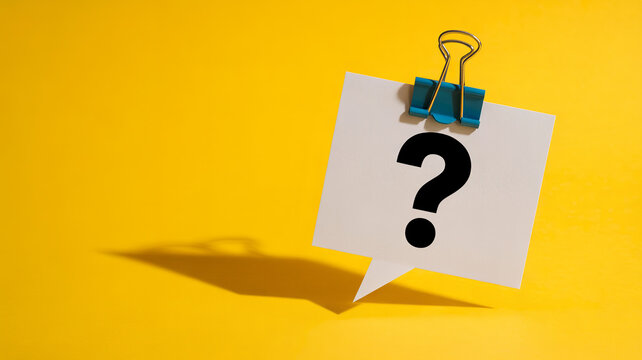 A question mark on a white speech bubble paper is held by a blue clip against a bright yellow background